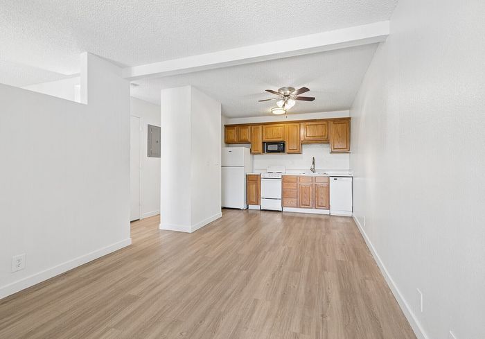 Bright modern kitchen with warm wood cabinetry, sleek appliances, and elegant ceiling fan, set against chic white walls and smooth laminate flooring.