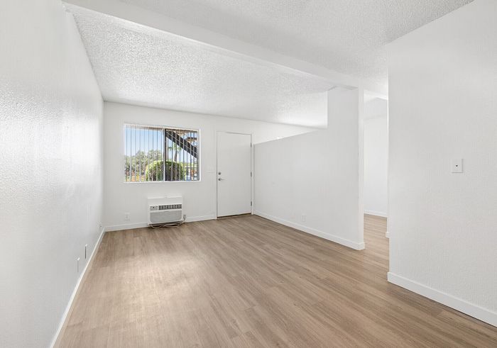 Bright and airy living space with modern hardwood floors, pristine white walls, and a large window offering natural light.