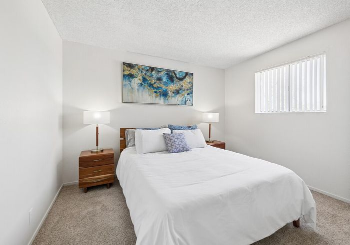 Bright and inviting bedroom with plush carpeting, featuring modern art and elegant wooden furniture.