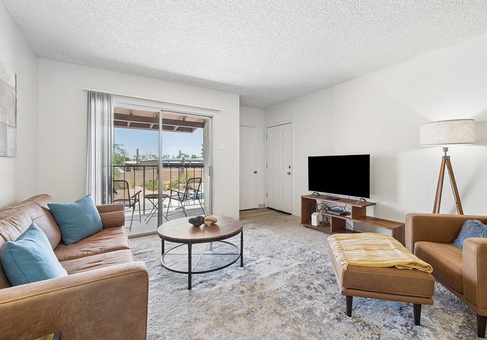 Bright living room with modern decor, featuring a cozy brown leather sofa, stylish armchair, open sliding doors leading to a scenic balcony view, and natural light enhancing the space.