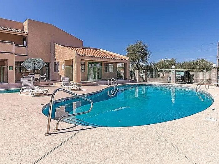 Inviting outdoor pool area with sun loungers and parasol against a backdrop of a stylish building under a clear blue sky.
