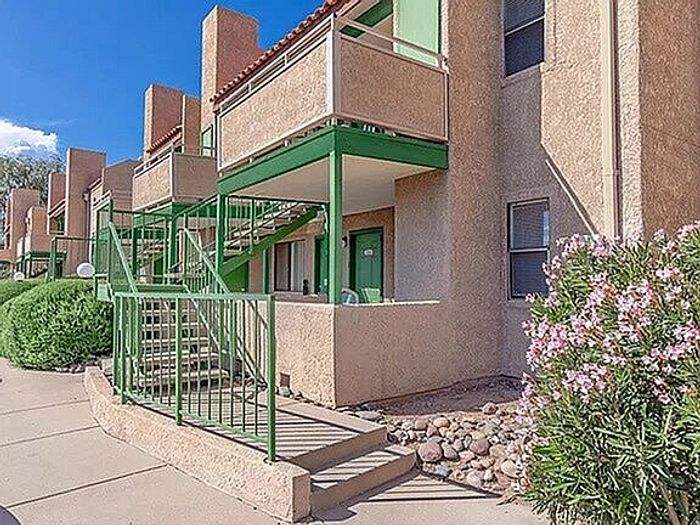 Charming apartment exterior with modern green railings, spacious balconies, and lush landscaping under a clear blue sky.