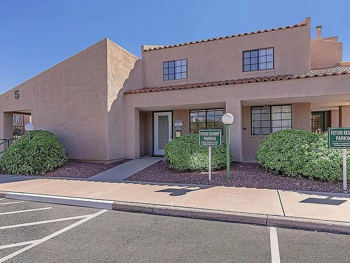 Charming adobe-style apartment complex with manicured shrubs and ample parking in a sunny setting.