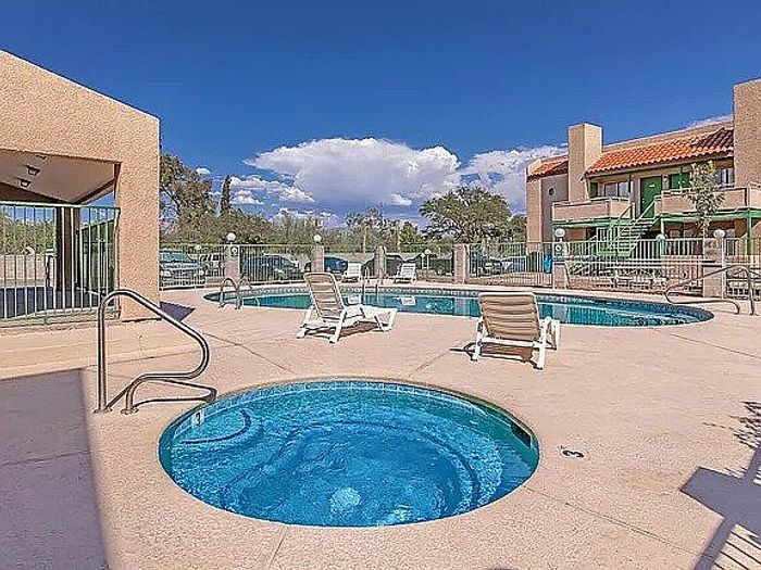 Inviting apartment complex with a sunlit pool and cozy hot tub, surrounded by a serene landscape and modern architecture.