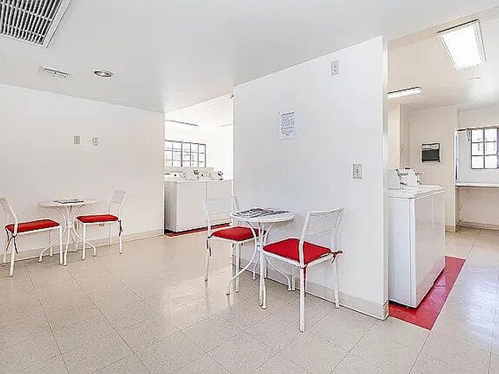 Bright and airy communal laundry room featuring modern washing machines and cozy seating areas with red-cushioned chairs.