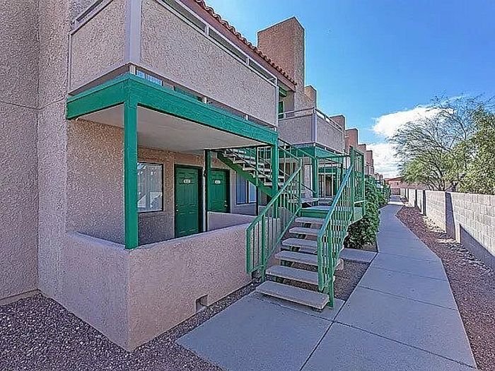 Charming apartment building with vibrant green railings and a welcoming exterior staircase, set against a clear blue sky.