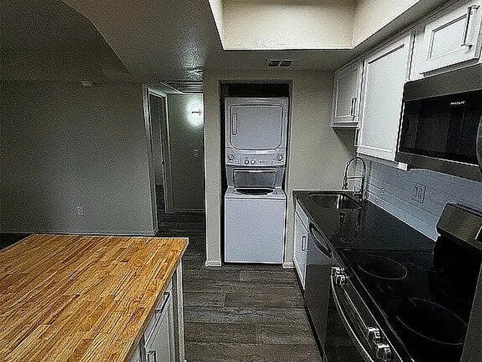 Modern kitchen with sleek appliances, wooden countertop island, and in-unit stacked washer and dryer.