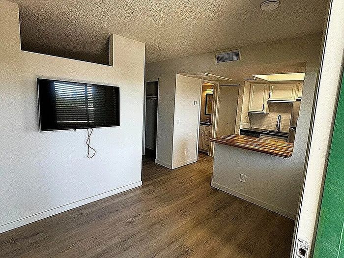 Modern apartment showcasing a sleek mounted TV, elegant hardwood flooring, and a charming kitchen with a wooden countertop.