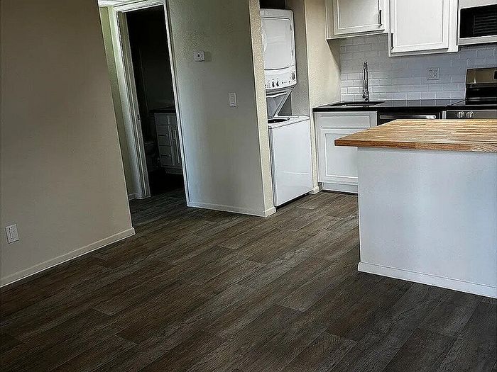 Modern kitchen with elegant white cabinetry, warm wood countertops, and in-unit laundry, featuring stylish dark wood flooring.