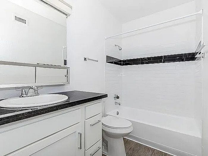 Modern bathroom with sleek black countertop, elegant mirror, and stylish tile accents over the bathtub.