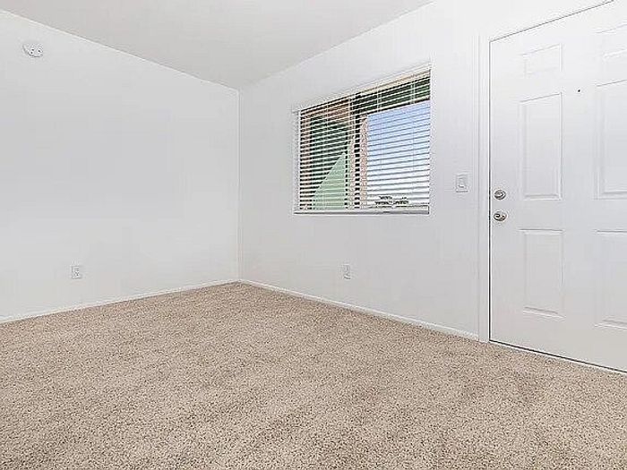 Inviting room with plush carpeting, large window with blinds, and fresh white walls in a cozy apartment.