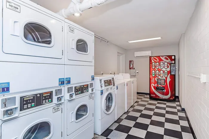 Modern laundry room with efficient washing and drying machines alongside a convenient soda vending machine, all set on a stylish black-and-white checkered floor.