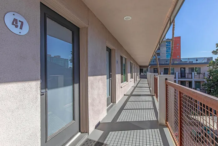 Sunlit corridor of a modern apartment complex with sleek glass doors, showcasing a vibrant urban living environment.