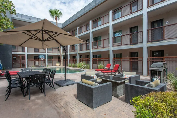 Chic apartment courtyard featuring outdoor seating, a stylish poolside lounge, and modern grill under a large umbrella perfect for relaxation and socializing.