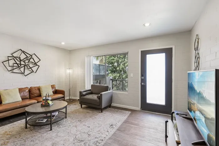 Bright and inviting modern living room with stylish decor, featuring a cozy leather sofa, armchair, and a large window offering lush greenery views.