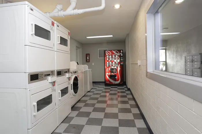 Modern laundry room featuring high-capacity washers and dryers with sleek design, alongside a convenient vending machine in a well-lit, tiled space.