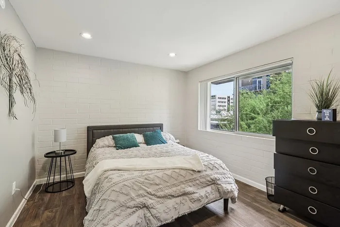 Bright and cozy bedroom with stylish decor, featuring a comfortable bed, modern dresser, and a large window offering natural light and a view of greenery.
