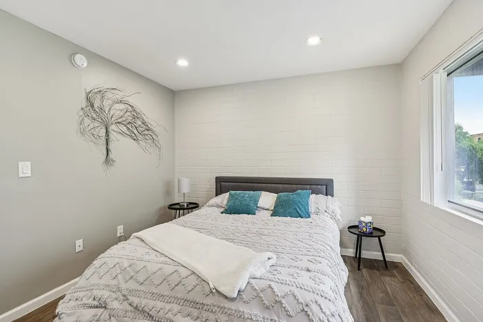 Bright, modern bedroom featuring a cozy bed with teal pillows, elegant wall decor, and ample natural light.