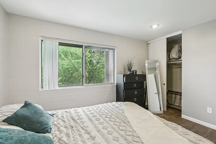 Bright and cozy bedroom with a large window offering lush green views, elegant decor, and a sleek storage dresser.