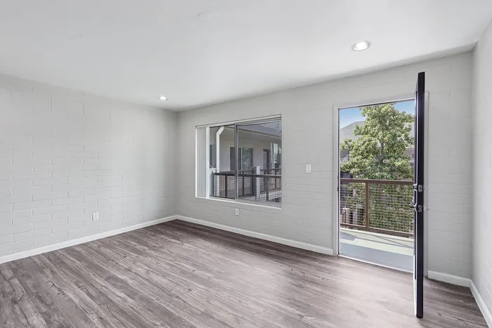 Bright and airy apartment space with elegant wood flooring, large window, and balcony access offering serene views.