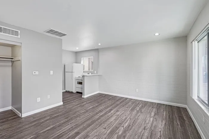 Bright, modern studio apartment with sleek hardwood floors, neutral gray walls, and natural light flooding through large windows.