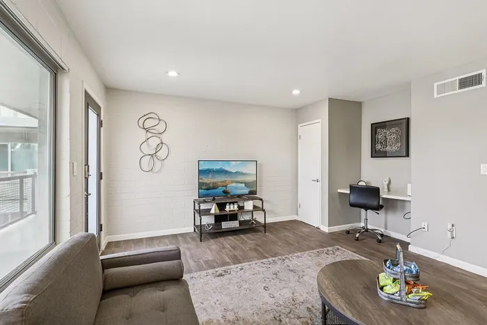 Bright and modern living room with elegant decor, featuring a cozy couch, sleek workspace, and a flat-screen TV, ideal for relaxation and entertainment.