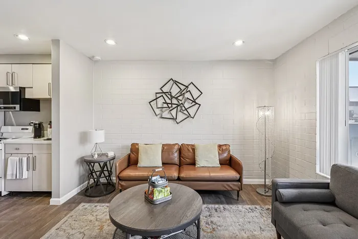 Sleek, modern living room with cozy leather sofa, artistic wall decor, and an elegant kitchen view, perfect for stylish urban living.