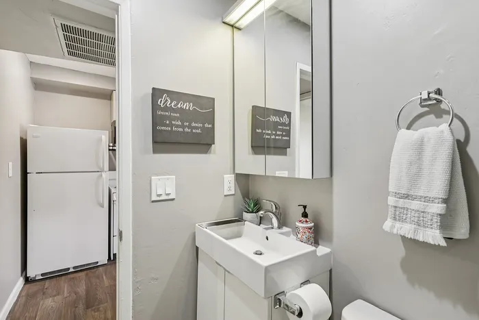 Charming bathroom with modern sink, soft lighting, and artful decor beside a compact kitchen area.