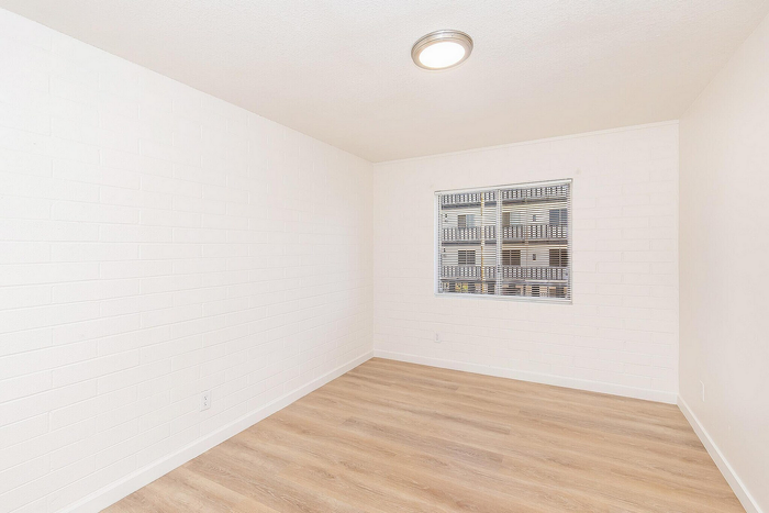 Bright and airy room with sleek white brick walls and elegant hardwood flooring, perfect for personalization and comfort.