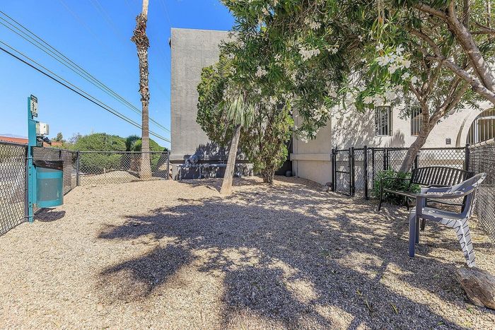 Charming outdoor area with lush greenery, featuring a cozy bench under the shade of vibrant trees and surrounded by a secure, fenced perimeter.