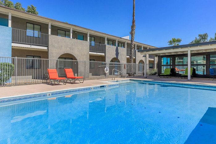 Sunlit apartment building with a sparkling swimming pool and vibrant red lounge chairs.