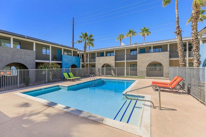 Charming apartment complex featuring a sparkling outdoor pool, vibrant lounge chairs, and lush palm trees, perfect for relaxation.