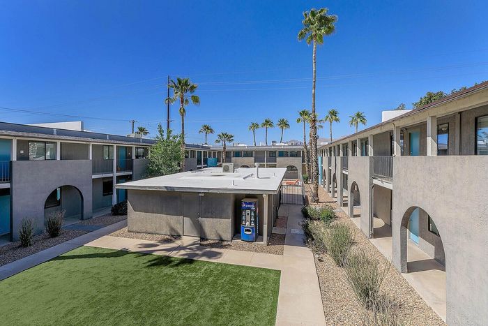 Modern apartment complex with palm trees, a well-maintained courtyard, and a bright blue sky backdrop.