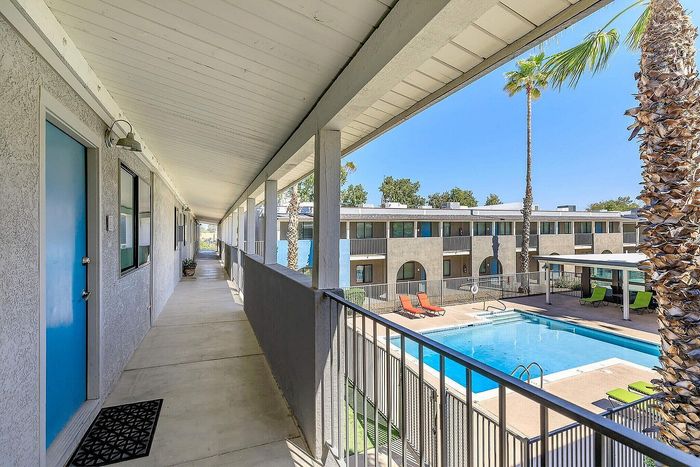 Inviting apartment complex with a charming poolside view, sunny lounge chairs, and lush palm trees, offering a perfect blend of relaxation and community living.