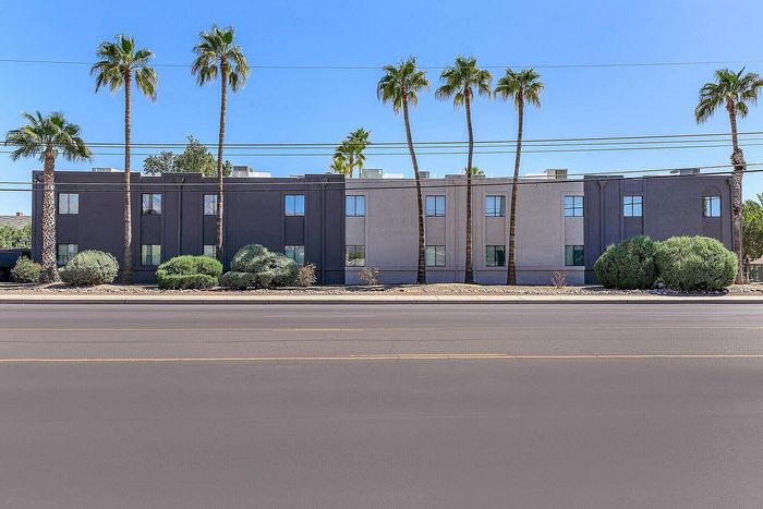 Modern apartment building facade with elegant architecture, framed by lush palm trees, under a clear blue sky.