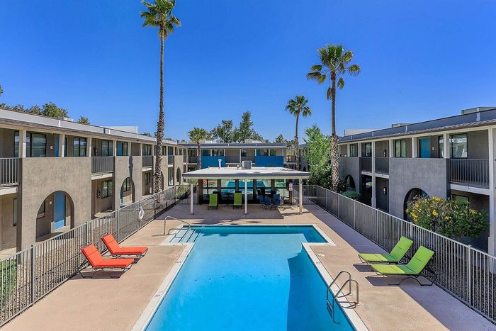 Inviting apartment complex with a sparkling pool, surrounded by modern two-story buildings and palm trees under a clear blue sky.