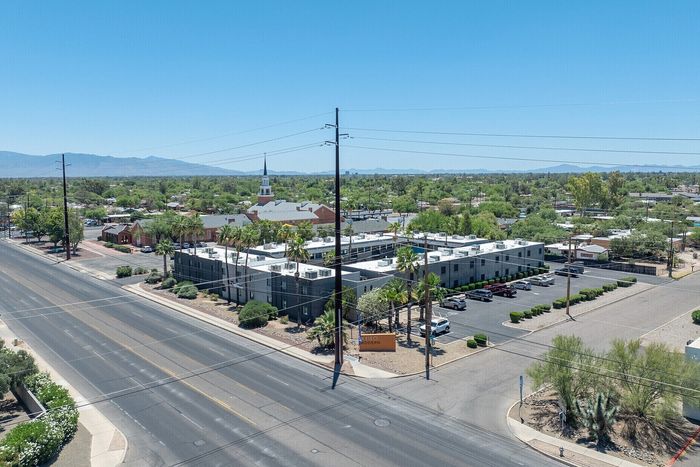 Aerial view of a modern apartment complex surrounded by lush greenery and palm trees, situated in a serene neighborhood with mountain views in the distance.