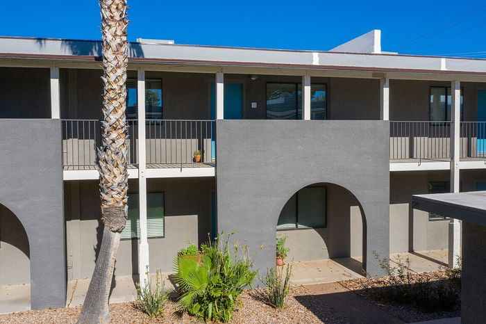 Modern two-story apartment complex with stylish arches, lush greenery, and a sunny courtyard.