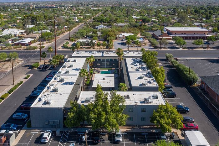Aerial view of a modern apartment complex with central courtyard and lush greenery, surrounded by picturesque desert landscape and mountain views.