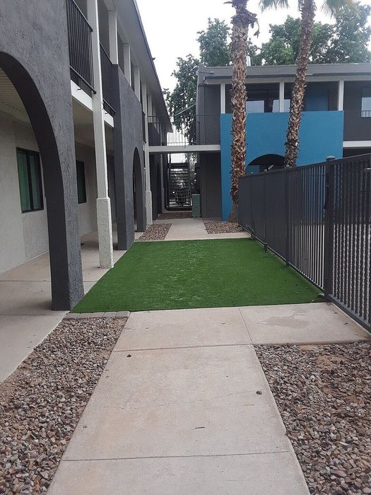 Charming apartment complex with modern arched architecture, vibrant blue accents, and lush green pathways lined with palm trees.