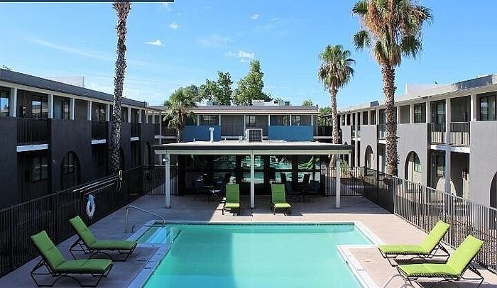 Modern apartment complex surrounding a refreshing swimming pool with stylish lounge chairs, lush palm trees, and contemporary architecture.