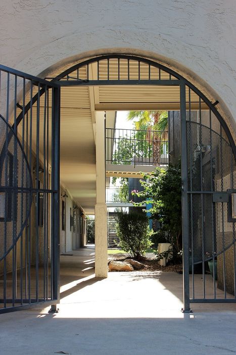 Elegant apartment entrance with wrought iron gates leading to a serene courtyard with lush greenery and modern architecture.
