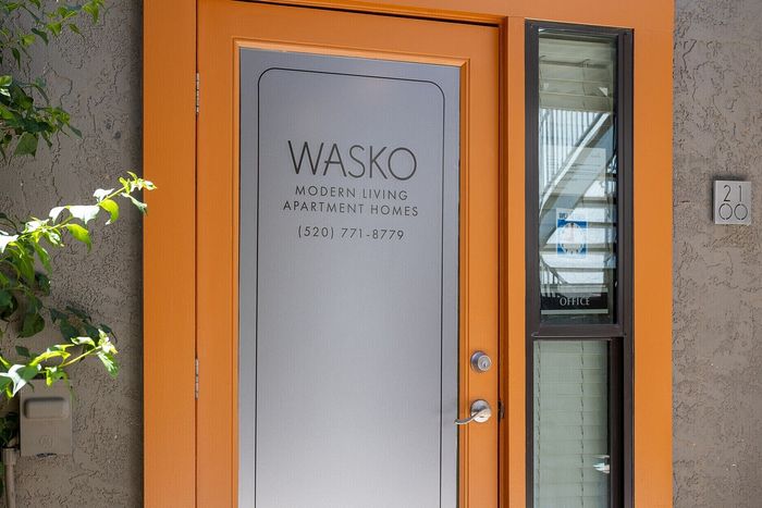 Chic entrance to Wasko Modern Living Apartment Homes, featuring a vibrant orange door and sleek design.