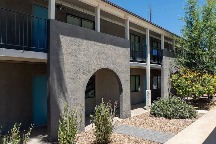 Charming two-story apartment complex with modern design, featuring blue doors, lush landscaping, and natural sunlight.