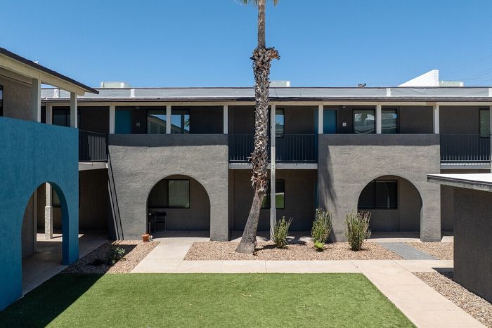 Charming apartment building with modern archways and lush courtyard under a clear blue sky.