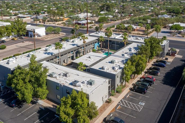 Aerial view of a modern apartment complex with ample parking, surrounded by lush greenery and showcasing a vibrant community area with a pool.