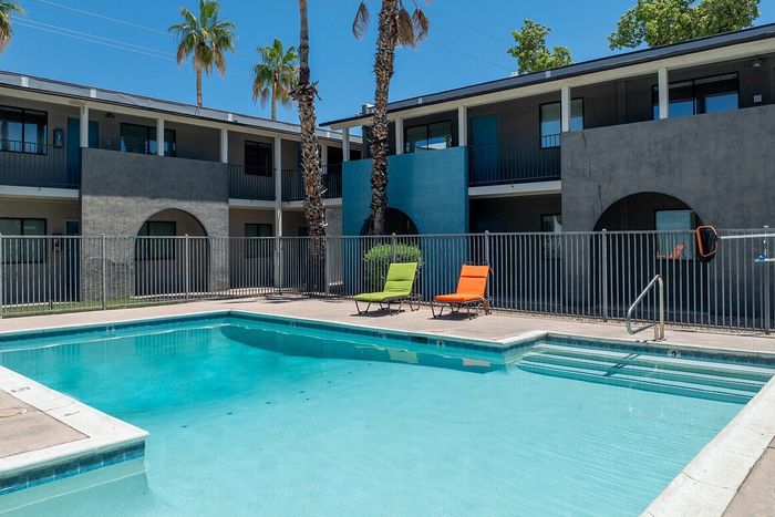 Inviting apartment complex with a crystal-clear swimming pool surrounded by vibrant lounge chairs and towering palm trees.