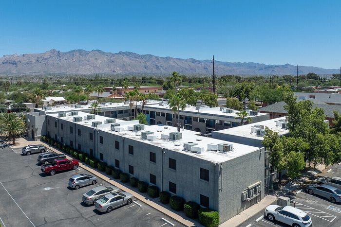Aerial view of a modern apartment complex with stunning mountain backdrop and ample parking.