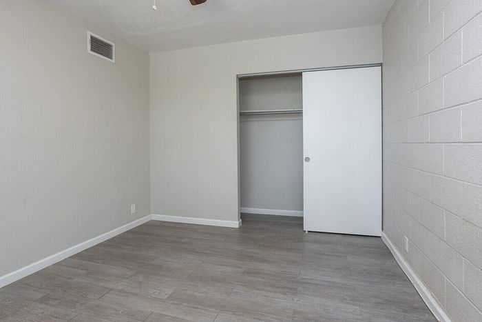 Modern apartment bedroom with sleek gray laminate flooring, neutral walls, and a spacious closet with sliding doors.