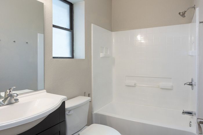 Bright and modern bathroom featuring a sleek vanity with mirror, a pristine bathtub, and a large window for natural light.